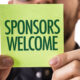 A sign on a post-it note held up by a corporate event executive saying sponsors welcome.