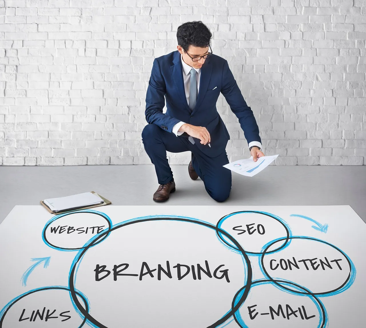 Businessman in a suit kneels by a diagram on the floor labeled with different event marketing and digital marketing channels.