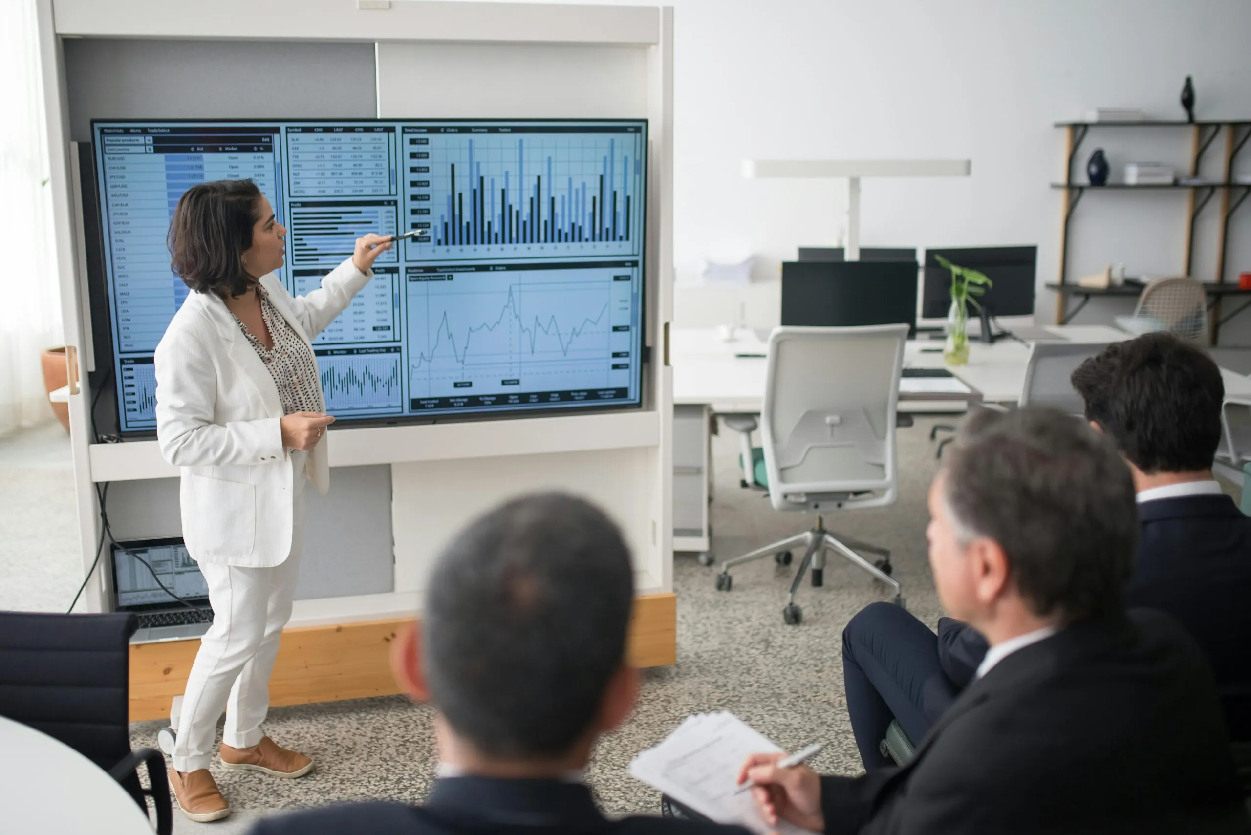 A woman in a white suit presents event marketing data on a large screen showing charts and graphs.