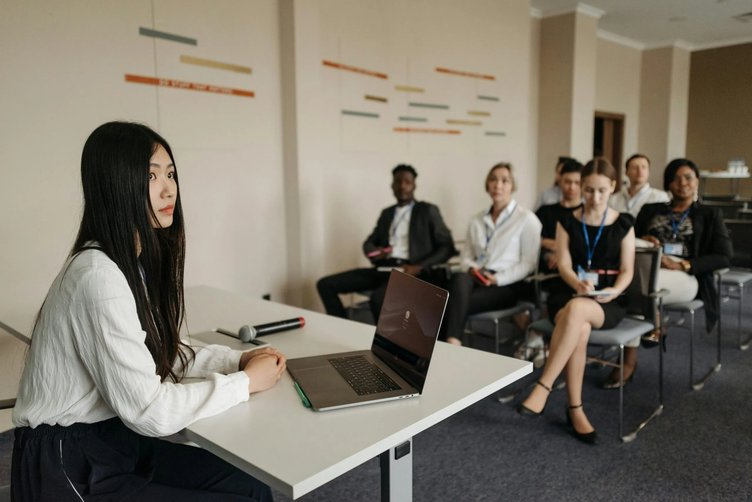 A diverse group of people in business attire attentively listening during an event marketing conference. They wear name tags and sit in rows with a laptop in the foreground.