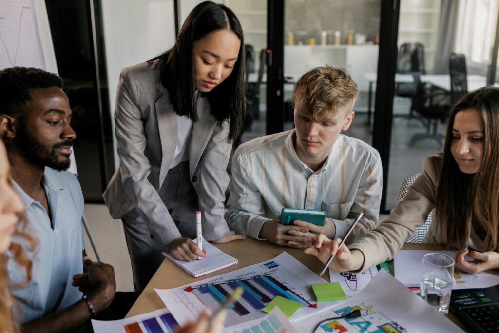 A diverse group of event marketing professionals collaborates in a bright office, reviewing colorful charts and notes on a table.