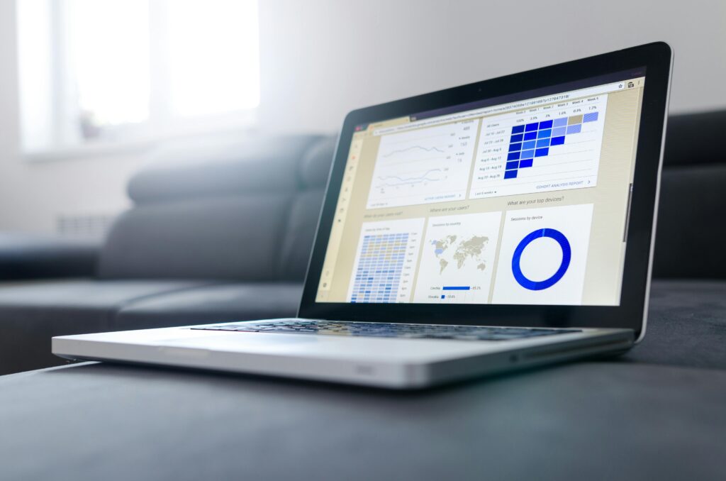 Open laptop displaying event marketing analytics dashboard with charts and graphs, set on a gray sofa. The screen shows line graphs, bar charts, and a pie chart.