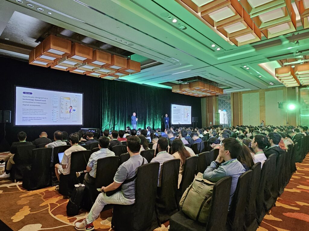 A large conference and seminar room filled with seated attendees facing a stage.