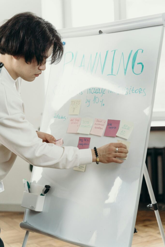 A person arranges colorful sticky notes on a whiteboard labeled "Planning," indicating strategic corporate event planning ideas to boost visitor numbers.