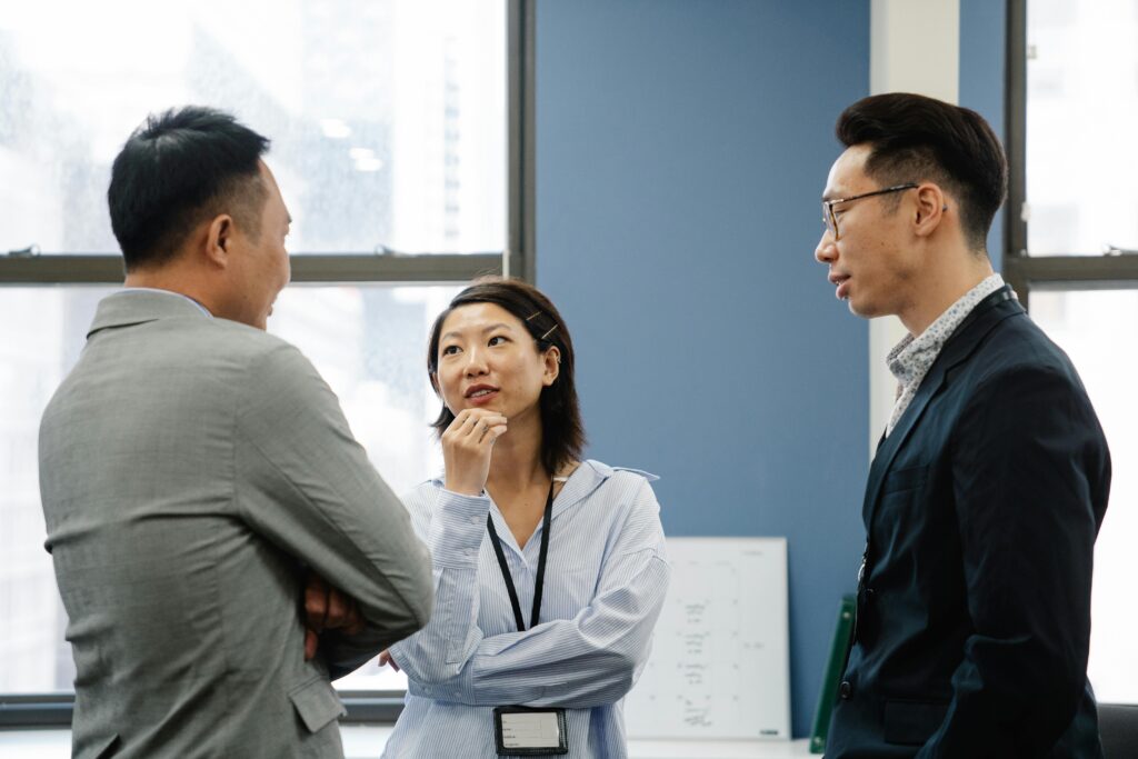 Three people engage in a thoughtful discussion at a networking event. One woman listens intently, while two men speak.